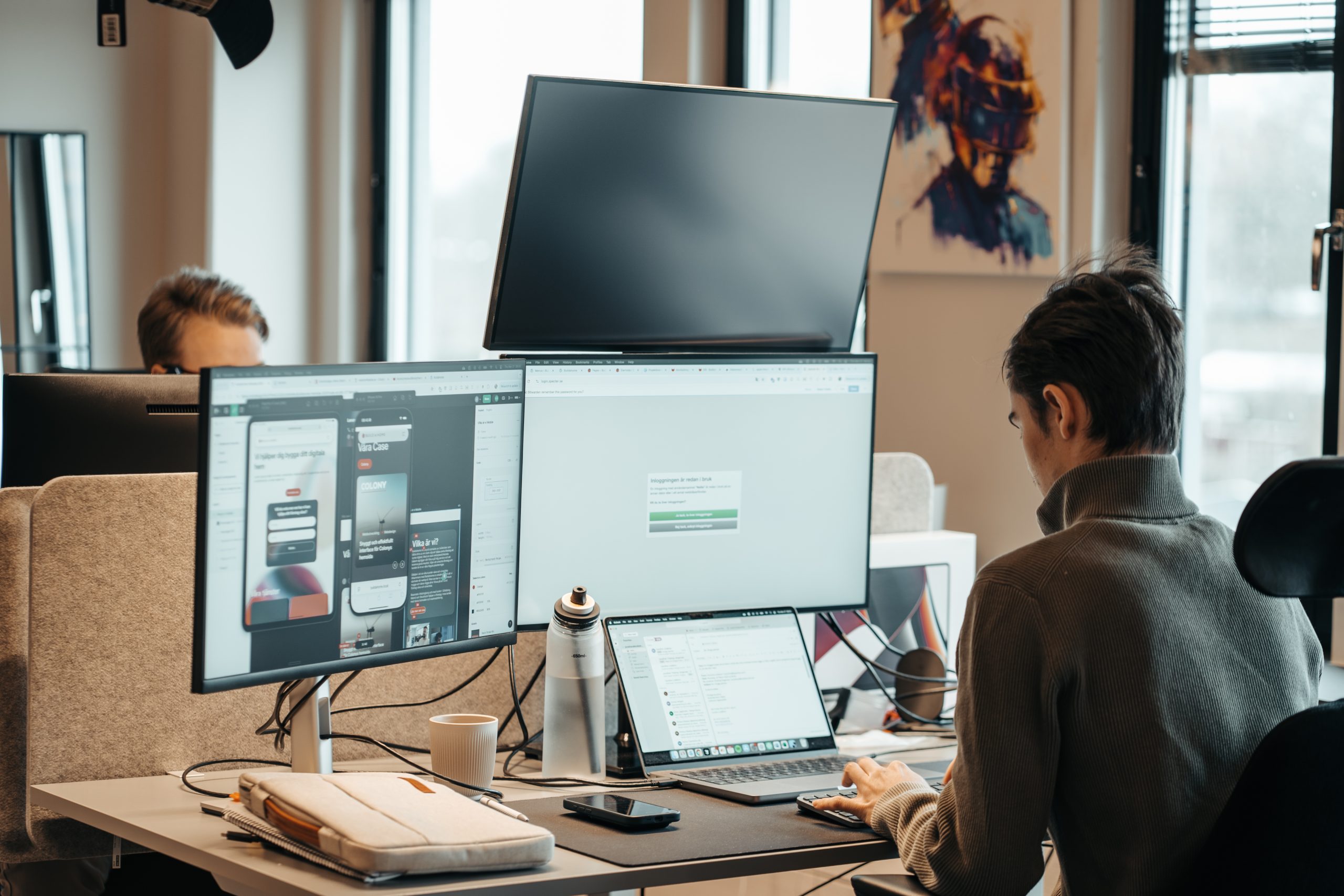 En kille sitter vid tre datorskärmar och en laptop